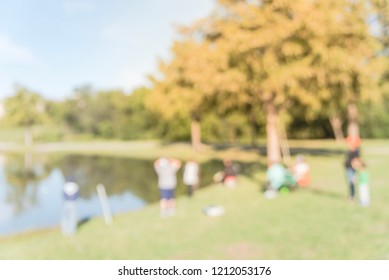 Blurred Family With Kids Fishing In Lake With Green Tree Lush. Free Community Event Sponsored By Neighborhood Association. Defocused People Fishing At The Lakeside Of Urban Park