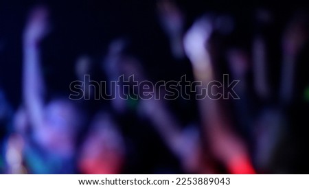 Blurred Fans Raise Hands and takes a photos in Front of Bright Colorful Strobing Lights on Stage.