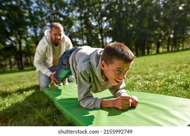 Blurred father helping teenage son with cerebral palsy doing plank exercise on fitness mat on green lawn in sunny park. Disability care and rehabilitation. Fatherhood and parenting. Sports lifestyle - Powered by Shutterstock