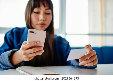 Blurred Female Student With Education Textbook Holding White Business Card And Using Smartphone Technology For Dialing Number, Woman Browsing Mobile Website While Checking Contact Information