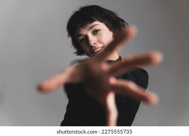 Blurred foreground. Woman reaching forward with her hand. Medium shot. Grey background. High quality photo