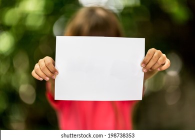 Blurred Girl Holding A Blank Piece Of Paper With Copy Space In Front Of Her.