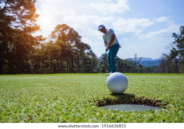 グリーンゴルフにボールを置くぼんだゴルファー、夕方の日差しレンズフレア。 ゴルフボールをホールに入れて、長い間勝つためのアクション。 