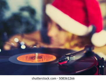 Blurred greeting card of Noel Christmas. Turntable vinyl record player. Sound technology DJ to mix & play music. Blurred a girl in Christmas cap with red hair listening to a vinyl record. Copy space - Powered by Shutterstock