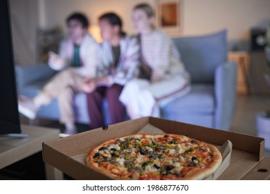 Blurred group of friends watching TV at home lit by blue light, focus on pizza in foreground, copy space - Powered by Shutterstock