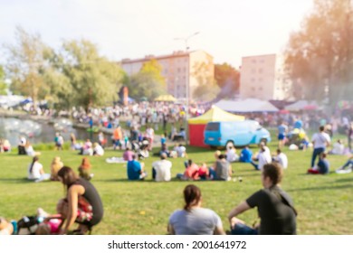 Blurred Group Of People, Family Members Enjoy Outdoor Picnic And Festival, Open-air Free Concert In Public Park. Audience Sits On Grass