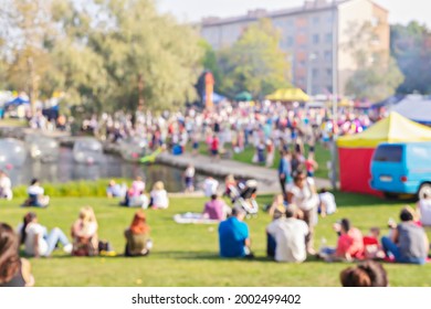 Blurred Group Of People, Family Members Enjoy Outdoor Picnic And Festival, Open-air Free Concert In Public Park. Audience Sits On Grass