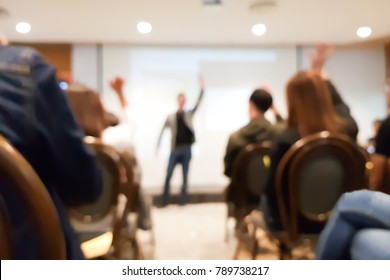 blurred group of people meeting in motivation seminar event at convention hall, speaker raising hand up and audience action follow , cheerful concept