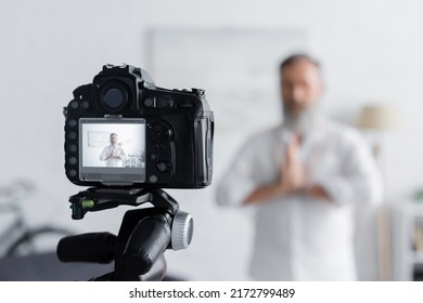 Blurred Guru Man Meditating With Praying Hands Near Digital Camera At Home