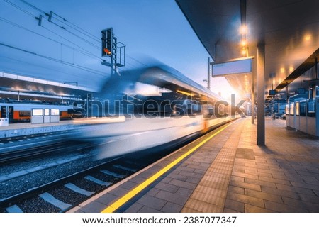 Blurred high speed train on the modern railway station at night in Graz, Austria. Fast moving intercity passenger train on the railway platform at sunset. Railroad. Passenger railway transportation