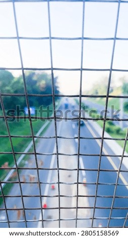 Blurred Highway View Through Wire Fence with Green Landscape and Urban Transportation Concept
