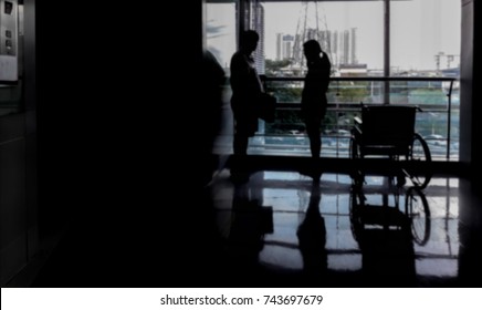 Blurred hospital image, Silhouette woman using mobile phone in front of window terrace near wheelchair and chubby man, Big guy waiting girlfriend talking with phone near elevator and black copy space