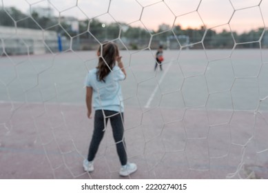 Blurred image. Back view of female child goalkeeper ready to catch a soccer ball stand on soccer field in football goal. Selective focus on girl. - Powered by Shutterstock