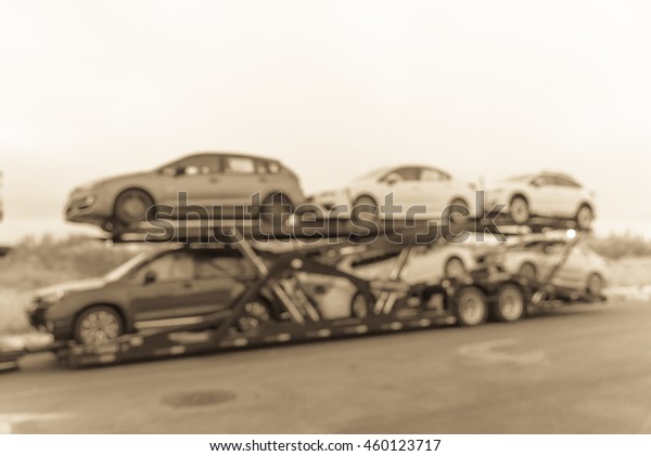 Blurred image big car carrier truck of new cars for\
batch delivery to dealership. Full load transport truck of new\
vehicles on country road. Automotive industry abstract\
background.Vintage filter\
look