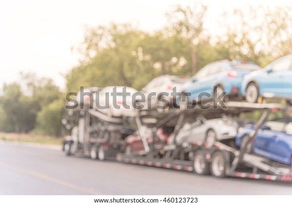 Blurred image big car carrier truck of new cars for\
batch delivery to dealership. Full load transport truck of new\
vehicles on country road. Automotive industry abstract\
background.Vintage filter\
look