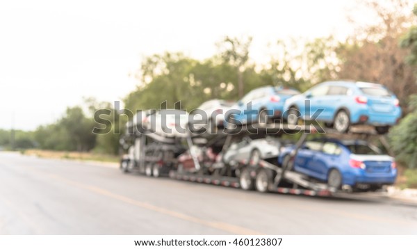 Blurred image a big car carrier truck of new cars\
for batch delivery to dealership. Full load transport truck of new\
vehicles on country road. Automotive industry abstract background.\
Panorama style.