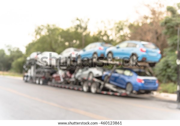 Blurred image big car carrier truck of new\
cars for batch delivery to dealership. Full load transport truck of\
new vehicles on country road in San Antonio, TX. Automotive\
industry abstract\
background.