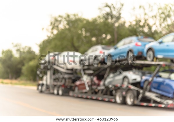 Blurred image big car carrier truck of new\
cars for batch delivery to dealership. Full load transport truck of\
new vehicles on country road in San Antonio, TX. Automotive\
industry abstract\
background.