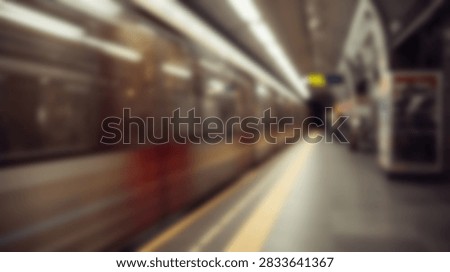 A blurred image captures the dynamic motion of a train arriving at a subway station platform, illuminated by bright overhead lights.