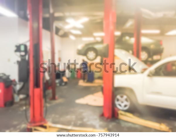 Blurred image of car in auto shop. Defocused
background of modern repair shop in Houston, Texas, US. Interior of
car repair shop with working Asian auto mechanic examining car
under hood.