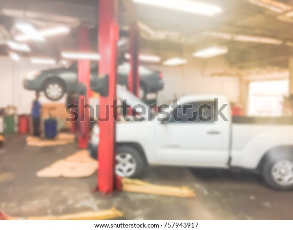 Blurred image of car in auto shop. Defocused\
background of modern repair shop in Houston, Texas, US. Interior of\
car repair shop with working Asian auto mechanic fixing under\
underneath car.