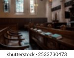 Blurred image of a church interior with wooden pews, stained glass windows, and hymnals. Church atmosphere, church seating, and church decor visible.