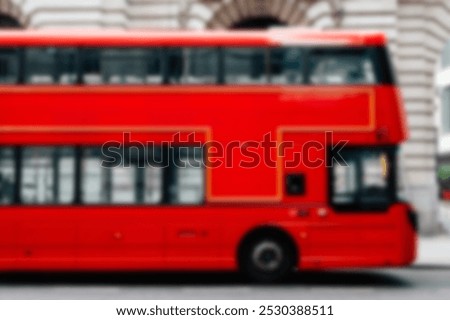 Blurred image of a classic red double-decker bus in an urban setting. The iconic red bus is a symbol of city transport and travel, often seen in busy streets. Red bus blurry background.