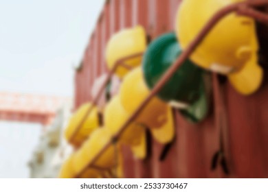 Blurred image of construction helmets hanging on a metal rod. Yellow and green helmets, safety gear, construction site, protective equipment, safety helmets. Construction site background. - Powered by Shutterstock