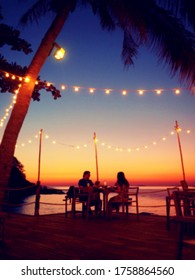 Blurred Image Of Couple Have Romantic Dinner At Beach With Sunset Sky Background