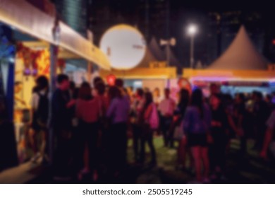 A blurred image of a crowded night market in Hong Kong, China. The scene is filled with brightly lit stalls and people, all moving and interacting with a bokeh background. - Powered by Shutterstock