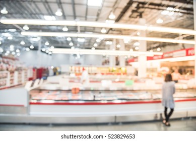 Blurred image customers shopping for fresh raw beef, pork, chicken, fish at meat department in wholesale store in US. Fully loaded shelves with variety of meat slices in boxes in a large supermarket.