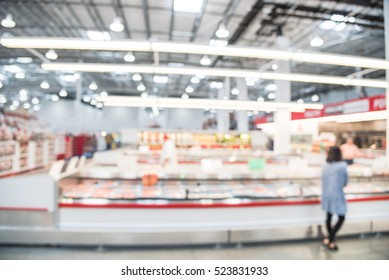 Blurred image customers shopping for fresh raw beef, pork, chicken, fish at meat department in wholesale store in US. Fully loaded shelves with variety of meat slices in boxes in a large supermarket.