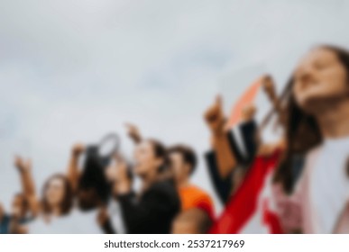 Blurred image of diverse group of people at a protest, holding signs and raising fists. Protesters, signs, and fists. Unity and activism. Diverse men and women protest outdoor against the sky - Powered by Shutterstock