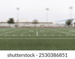 Blurred image of an empty football field with goalposts and bleachers. Football field with grass, goalposts, and bleachers. Overcast sky above the field. Football field and grass. Sport background