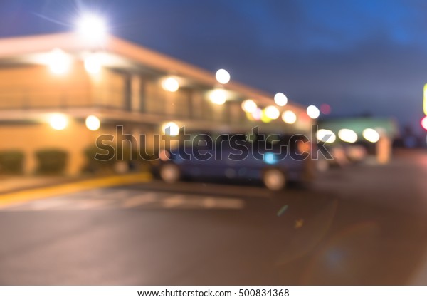Blurred image entrance of two story motel with\
parking lot in foreground at blue hour in Hope, Arkansas, US.\
Generic budget motel in suburban roadside location with row of\
parked cars next to\
rooms.