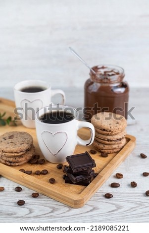 Blurred image of espresso cups, pieces of chocolate and cookies, jars of chocolate paste on a light table on a wooden tray. Coffee drinking concept.