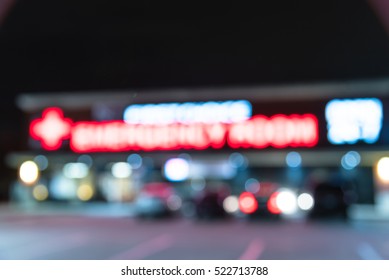 Blurred Image Exterior Emergency Room With Neon Led Sign Illuminated At Night In Houston, Texas, US. Facade Of Emergency Department With Neon Shining Signboard And Car Park. Healthcare Service Concept