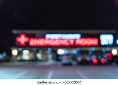 Blurred Image Exterior Emergency Room With Neon Led Sign Illuminated At Night In Houston, Texas, US. Facade Of Emergency Department With Neon Shining Signboard And Car Park. Healthcare Service Concept