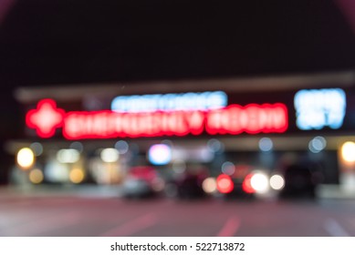 Blurred Image Exterior Emergency Room With Neon Led Sign Illuminated At Night In Houston, Texas, US. Facade Of Emergency Department With Neon Shining Signboard And Car Park. Healthcare Service Concept