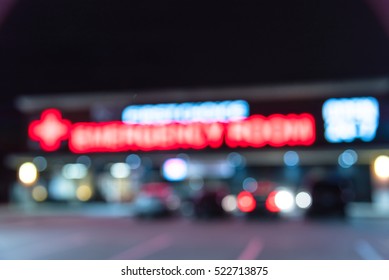 Blurred Image Exterior Emergency Room With Neon Led Sign Illuminated At Night In Houston, Texas, US. Facade Of Emergency Department With Neon Shining Signboard And Car Park. Healthcare Service Concept