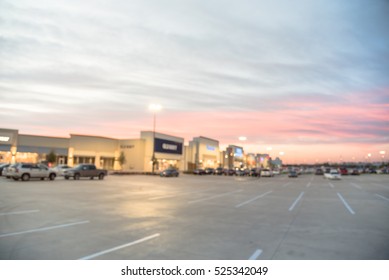Blurred image exterior view of empty parking lots in modern shopping center in Humble, Texas, US at sunset. Mall complex outdoor uncovered parking and bokeh light of retail store in background.