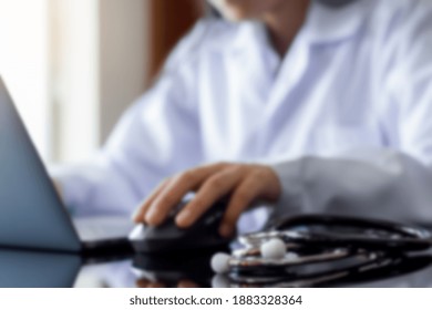 Blurred Image Of Female Doctor Hand Using Wireless Mouse And Work On Laptop Computer With Medical Stethoscope On The Table At Office. Telehealth, Telemedicine, Emr, Ehr Or Online Medical Concept.