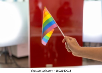 Blurred Image Of A Flag Of Lesbian, Gay, Bisexual, And Transgender Or LGBT Flag Being Held By A Hand In A Business Office