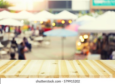 Blurred Image Of Food Fairs And Food Festivals Consist Of Many Booth And Vendors At Food Stalls. People Walking In Street. Event In Chiang Mai At Twilight Montage With Wood Table Top For Background.