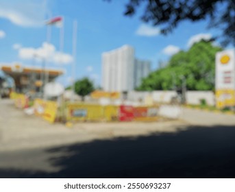 A blurred image of a gas station with vibrant yellow branding, construction barriers, and a modern high-rise building in the background - Powered by Shutterstock