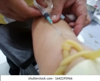 Blurred Image Of Hands Medical Technician Pricking Needle Syringe In The Arm Patient Drawing Blood Sample For Blood Test, Puncture Of A Vein Through The Skin In Order To Withdraw Blood For Analysis.