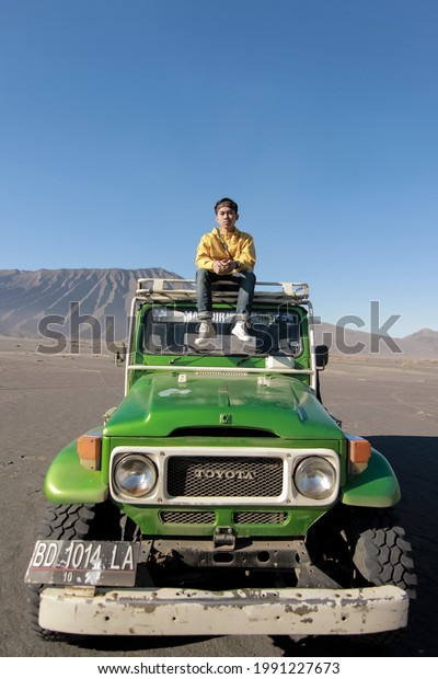 Blurred image of hardtop car and tour guide in Bromo\
Tengger Semeru National Park. a beautiful view of a jeep with a\
widodaren hill in the background and blue sky. East Java, Indonesia\
- juni 2021