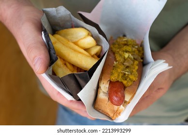 Blurred Image Of Hot Dog And Fried Potatoes In Hands. Street Food Concept.