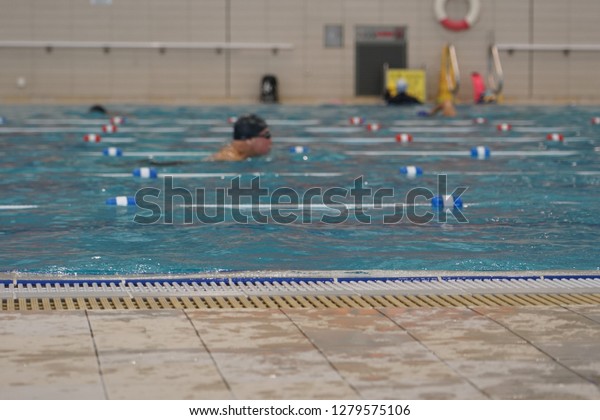 The blurred image of the indoor public\
swiming pool with some swimmers in the\
water.
