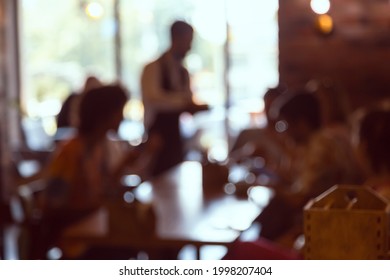 Blurred Image Of The Interior Of A Cafe And A Waiter Taking Orders From Customers. Defocused Photo For Design Needs